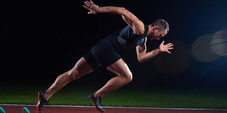 Athlete sprinting on track at night, displaying speed and power.