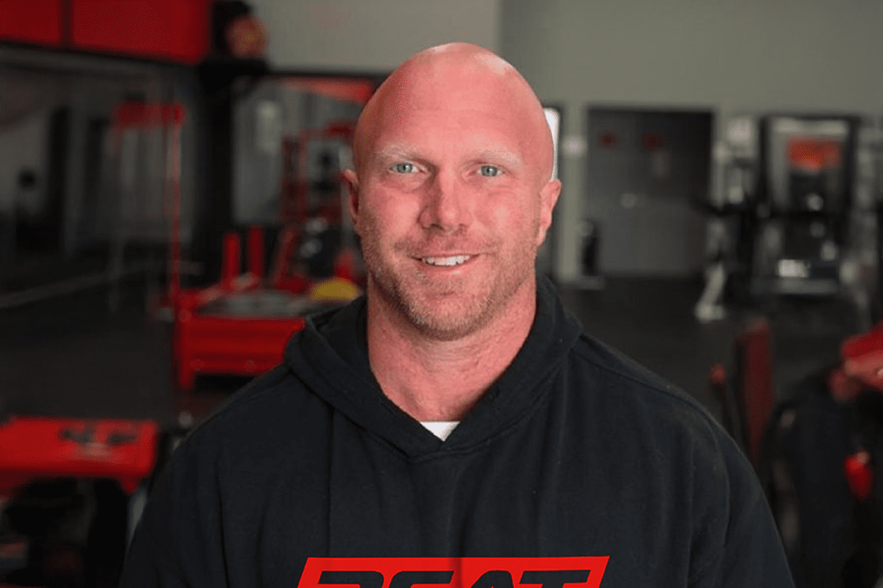 Bald man in a hoodie smiling in a gym setting.