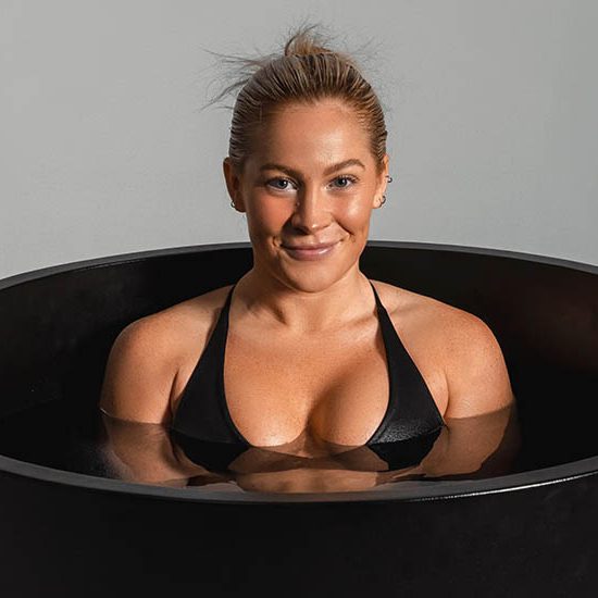 Person in a black bikini top smiling in a cold plunge tub.