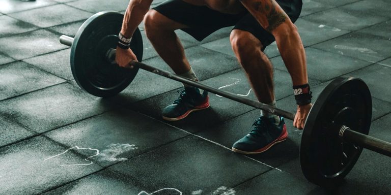 Man performing a deadlift in gym with barbell and weights on rubber floor.