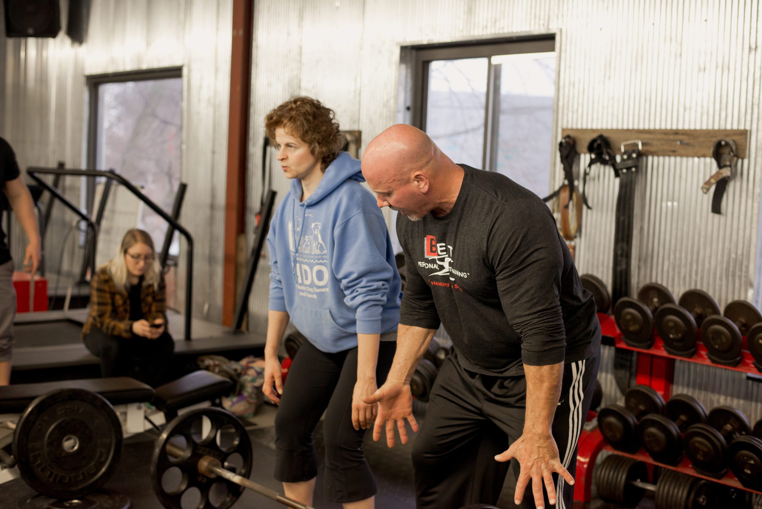 Trainer guides woman on deadlift technique in gym.