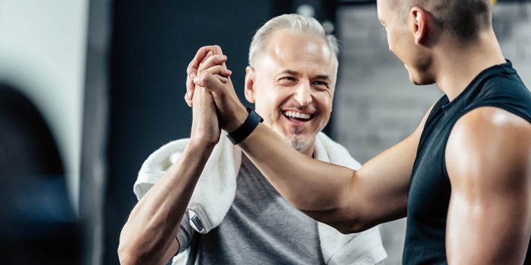 Two men in a gym high-five and smile after a workout session.