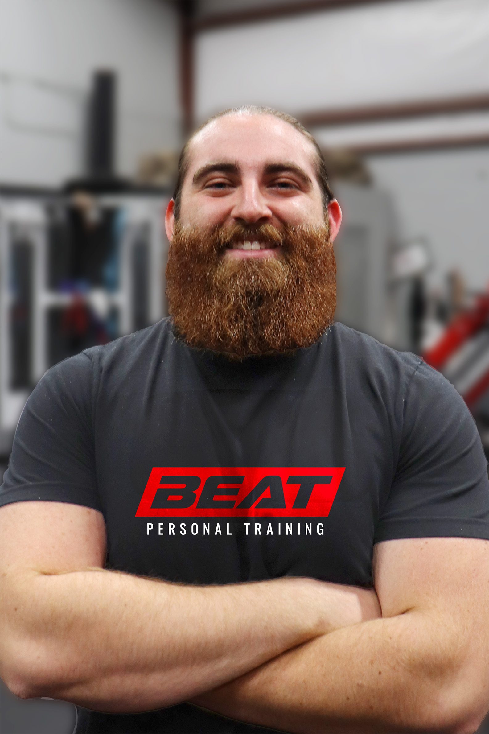 Personal trainer with beard standing confidently in gym, arms crossed.
