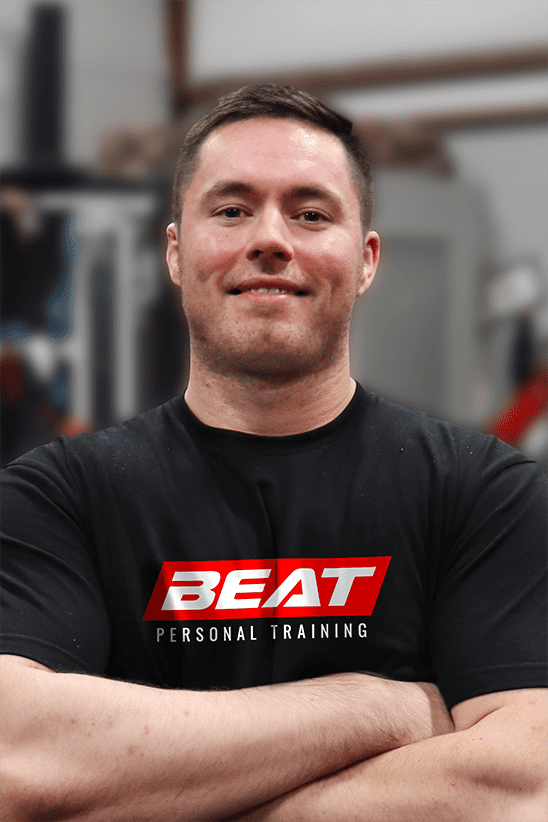 Man in Beat Personal Training shirt, smiling confidently in gym setting.