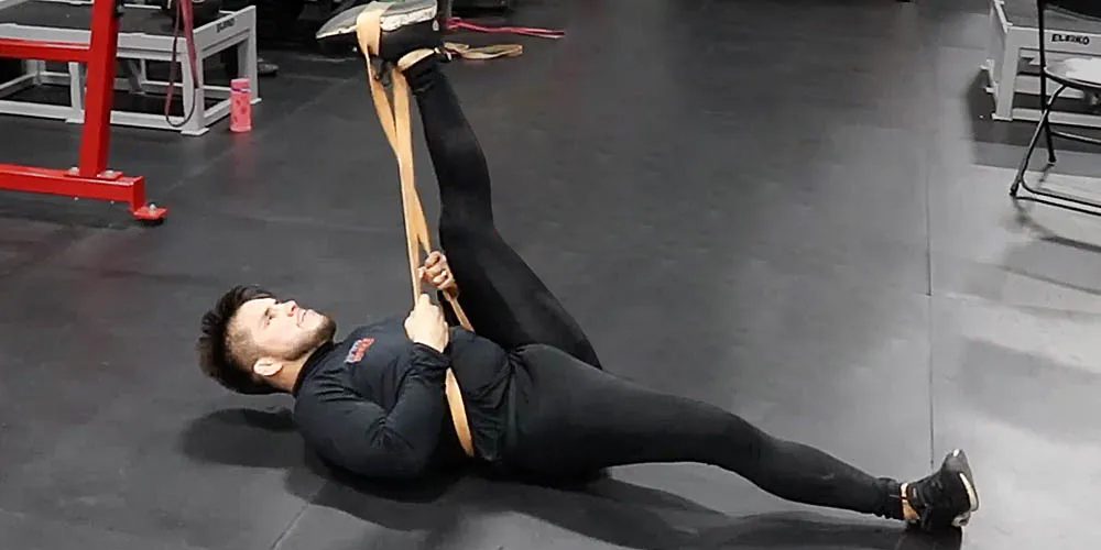 Man stretching with resistance band at gym on black mat.
