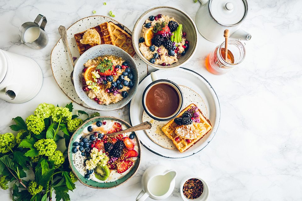 Healthy breakfast with waffles, oatmeal, berries, and tea on a marble table.