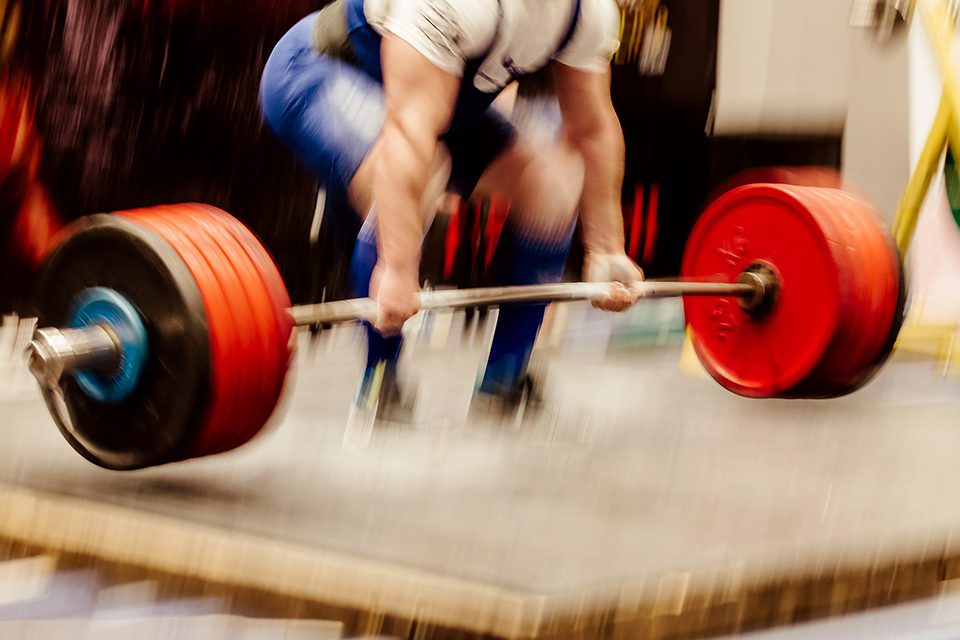 Powerlifter performing a deadlift with red weight plates in a gym.